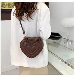Deep brown heart-quilted crossbody bag with ruffled edges shown on a fashion model