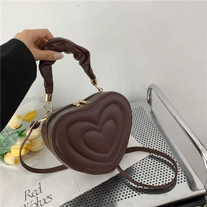 Detail of dark brown heart-shaped crossbody bag with ruffled handle and metal zipper