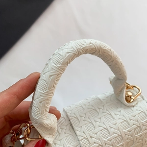 Detail of white woven leather handbag featuring gold metal hardware and a curved handle