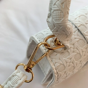 Close-up of white woven leather texture with shiny gold metal lobster clasp and D-ring