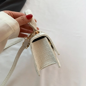 Detailed side view of white mini handbag showing woven texture and gold hardware details