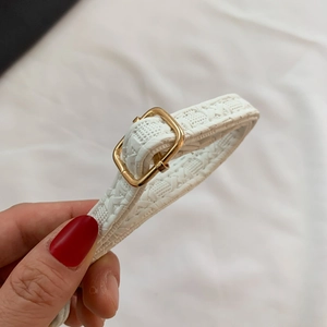 Close-up of white woven faux leather belt with a polished gold square metal buckle