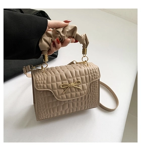 Detail of khaki croc-embossed handbag featuring a gold bow buckle and pleated handle