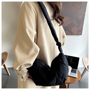 Close-up of black quilted puffer hobo bag with knotted strap on model in beige coat