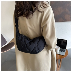 Detail of a black quilted heart-patterned shoulder bag worn over a classic beige trench coat