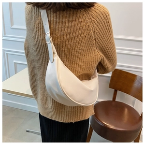 Detail showing cream semi-circle crossbody bag with adjustable strap on brown sweater