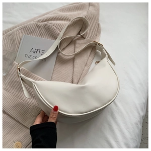 Detail of a creamy white crescent bag with gold metal hardware and a wide shoulder strap