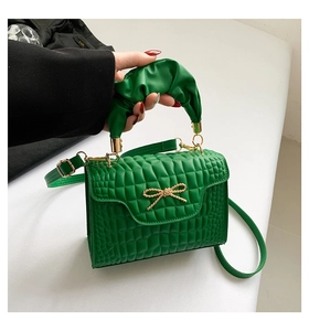 Detail of green faux-crocodile handbag with gold bow hardware and pleated handle strap