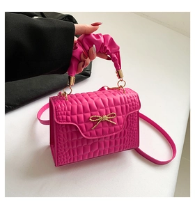 Detail of pink croc-embossed handbag with golden bow hardware and ruched handle