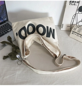 Detail of canvas tote bag featuring MOOD text and a cute green frog plush keychain charm