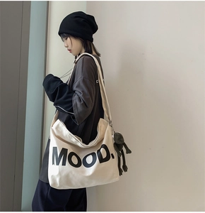 Close-up of a large off-white canvas tote bag with MOOD lettering and a green frog pendant