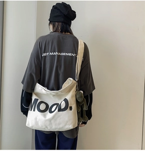 Back view of model wearing a large white canvas shoulder bag with Mood. text and frog charm