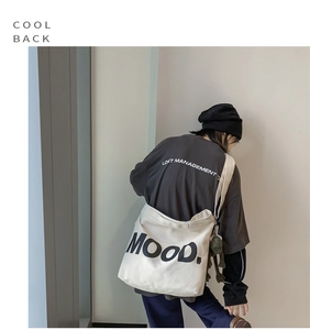 Model wearing a large cream canvas shoulder bag with MOOD print in a casual style