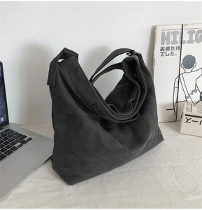 Large black canvas tote bag with letter print shown next to laptop and magazine
