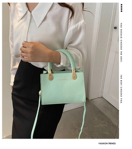 Detail view of mint green crocodile-texture handbag with a unique woven handle and gold lettering