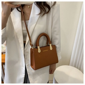 Detail of brown crocodile embossed crossbody bag with woven handle and gold lettering