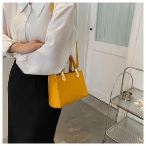 Close-up of bright yellow textured handbag with gold hardware and woven handle