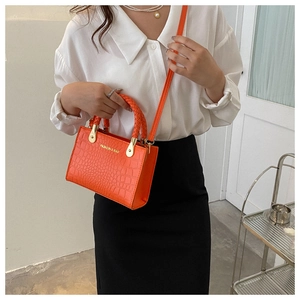 Detail of bright orange handbag featuring crocodile texture and woven top handles