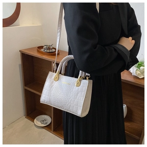 Close-up of white crocodile pattern handbag featuring a braided handle and gold brand logo