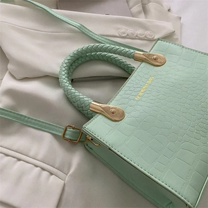 Detail of mint green crocodile pattern bag with woven handle and gold hardware