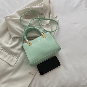Detailed flat lay of mint green crocodile pattern handbag with woven handle and strap