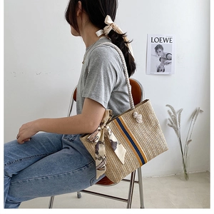 Detail of hand-woven straw tote with striped pattern and decorative printed silk scarf