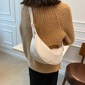 Minimalist beige crescent saddle bag with wide shoulder strap in a daily street style