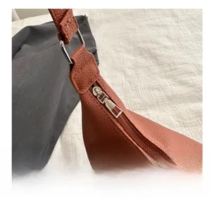 Détail de la fermeture éclair argentée et du cuir marron sur le sac à bandoulière