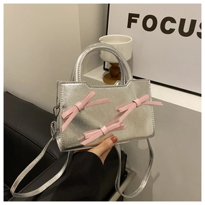 Détail d'un mini sac à main argenté avec des nœuds roses, tenu à la main avec style