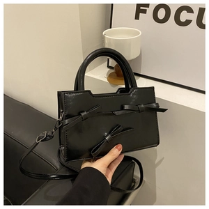 Détail du sac à main noir à nœuds papillon avec finition brillante et bandoulière