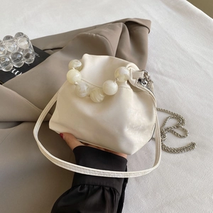 Detail of macaron pearl cloud bag showing marble sphere handle and chain strap on cream leather