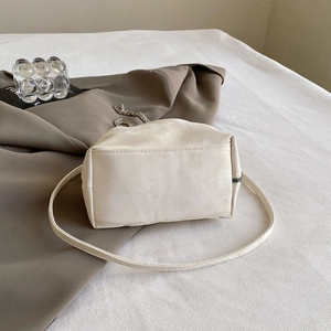 Macro detail of creamy white matte cloud bag with silver chain on soft fabric