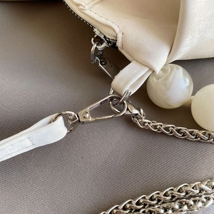 Close-up of white crossbody cloud bag with silver chain and marble texture beads
