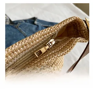 Detailed close-up of a smooth gold metal zipper and brown strap on a beige straw bag