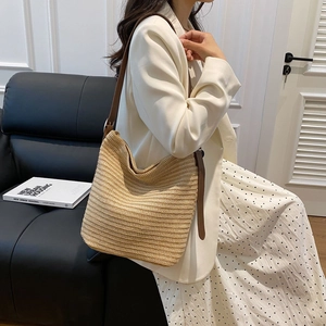 Detail of a large straw shoulder bag with leather straps on a model in a cozy interior