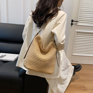 Detail of hand-woven straw shoulder bag with dark brown leather strap worn by a model