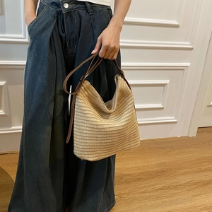 Detail of a large woven straw shoulder bag with brown leather handles and textured pattern