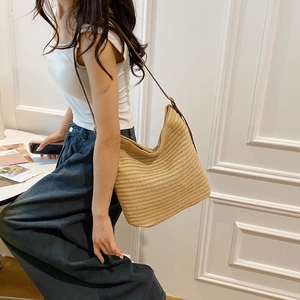 Detail of straw woven hobo bag with brown leather strap worn by a model in casual style