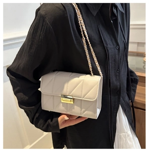 Détail d'un petit sac carré blanc cassé avec surpiqûres en V et bandoulière chaîne dorée