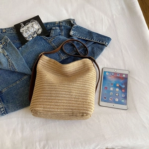 Flat lay view of a large straw tote bag with a brown leather strap and lifestyle props