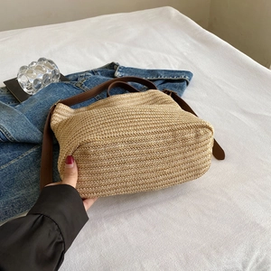 Flat lay of a woven straw shoulder bag with brown leather straps on white bedding