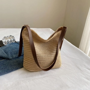 Detail of straw tote bag showing beige woven texture and dark brown leather strap