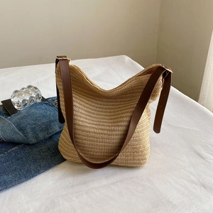 Detail of woven straw shoulder bag featuring adjustable brown leather strap and metal buckle