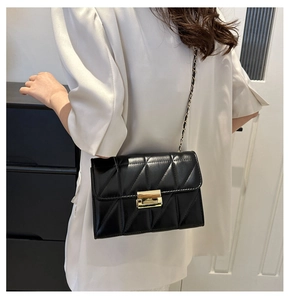 Détail d'un sac bandoulière noir matelassé avec chaîne dorée porté par un mannequin