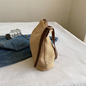 Detail of hand-woven straw tote with dark brown leather strap and gold buckle hardware