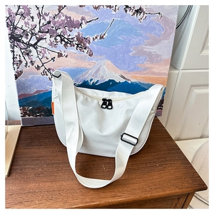 Close-up of a white waterproof nylon crescent crossbody bag with black zippers on wood