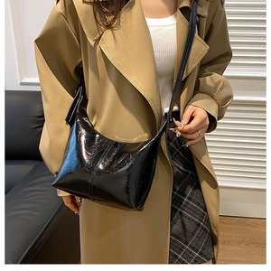 Close-up of a glossy black crescent shoulder bag styled with a classic trench coat