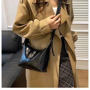 Glossy black leather crescent hobo bag shown as a shoulder bag on a model in trench coat