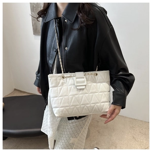 Dettaglio di una borsa a spalla trapuntata beige con tracolla a catena indossata da modella