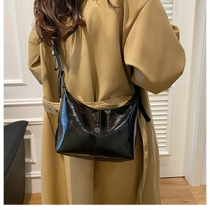 Detail of glossy black wrinkled leather texture on a crescent shoulder bag worn by model
